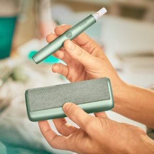 A Jade Green IQOS ILUMA PRIME Holder and Pocket Charger in a person's hands.