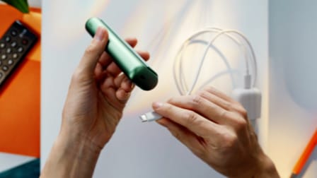 A charging cable being inserted into an IQOS ILUMA PRIME holder.