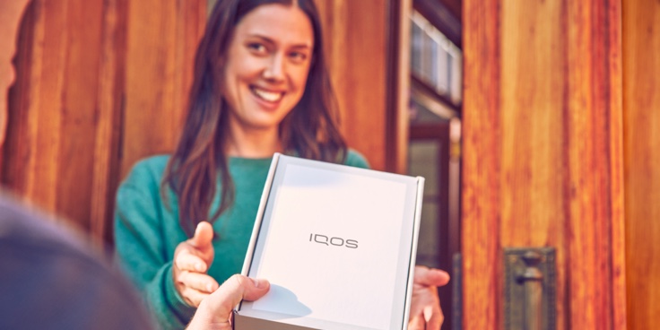 One person handing an IQOS device box to a smiling woman.