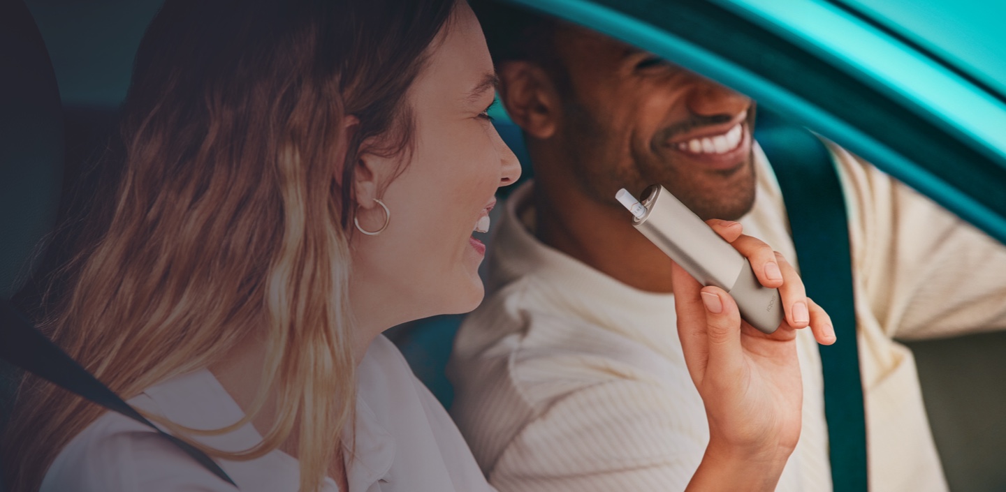 A person using an IQOS device laughing with two other people.