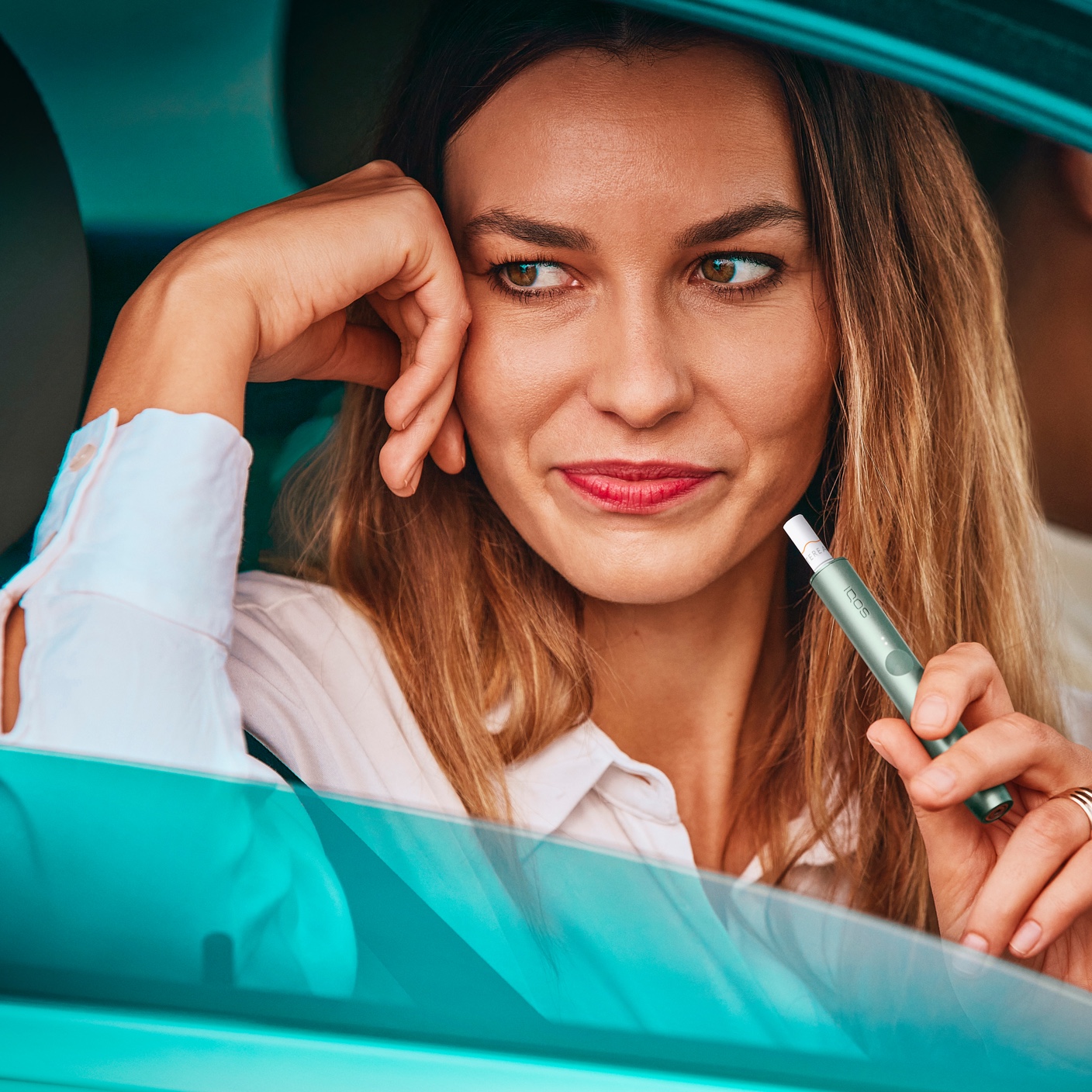 A woman uses an IQOS ILUMA device while sitting in a car.