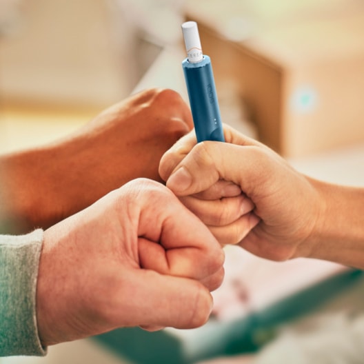 Two people fist bumping; one holds and IQOS ILUMA device.