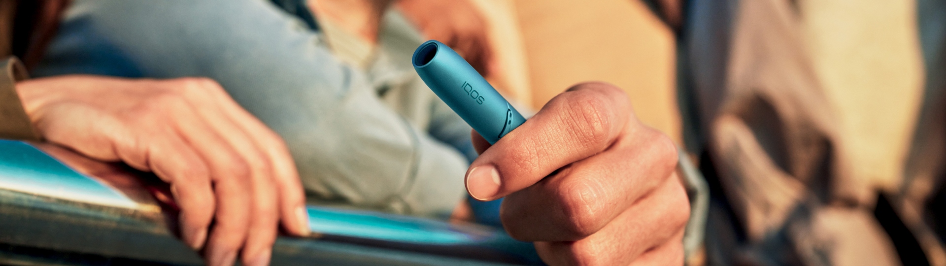 Woman smiling while holding IQOS ORIGINALS ONE in turquoise color.
