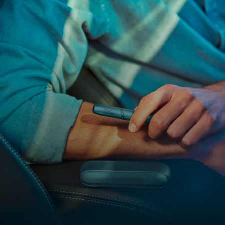 Man holding IQOS Originals One heated tobacco device in turquoise color while talking.