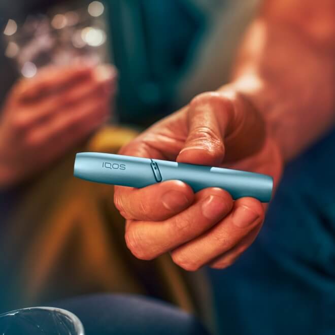 Hand holding IQOS Originals Duo holder in turquoise color.