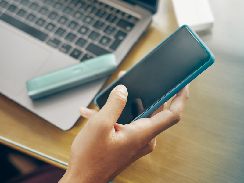 Hand holding a mobile phone, upgrading IQOS Originals ONE heated tobacco device firmware. 