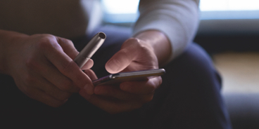 Person with a IQOS holder and a mobile in his hands in the dark